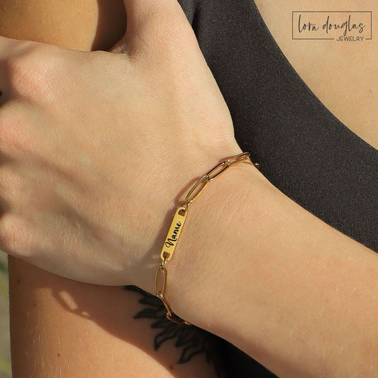Gold bracelet with engraved name on wrist, Lora Douglas Jewelry branding.