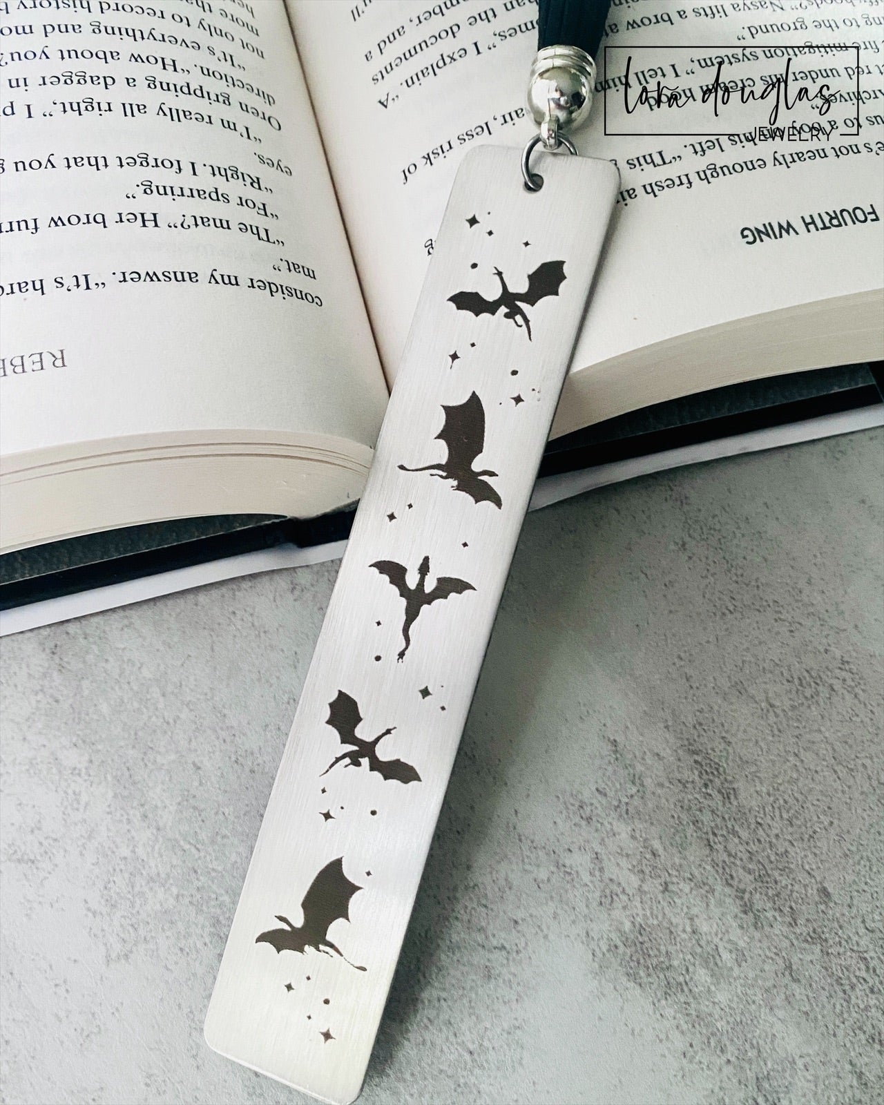 Silver stainless steel bookmark with engraved dragons sitting beside a copy of Fourth Wing Novel