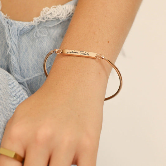 gold bracelet with engraved text on a wrist against a neutral background