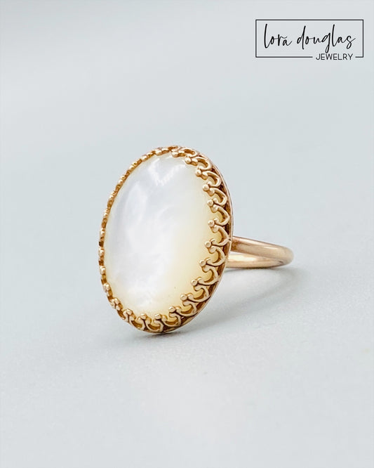 Close view of a natural Mother of Pearl stone set in a bronze ring. The 18 x 13 mm iridescent shell creates a luminous focal point in this size 6 statement ring for women who love unique artisan jewelry.