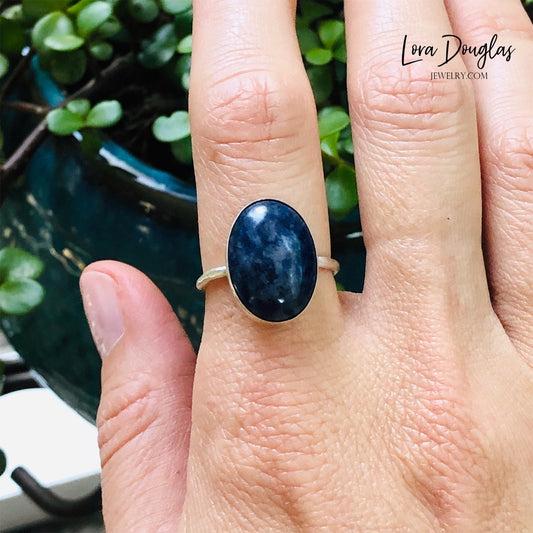 A sterling silver sodalite ring on a woman's finger, with a close-up on the ring showing the blue sodalite stone surrounded by a silver band.