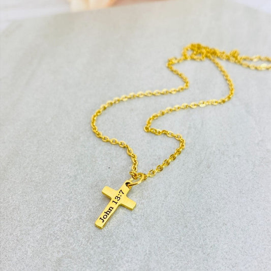 A gold stainless steel engraved cross necklace with a lobster clasp and a small cross charm, placed on a white surface