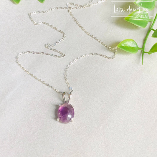 A sterling silver pendant necklace with a hand-cut amethyst gemstone, displayed on a silver chain against a black background.