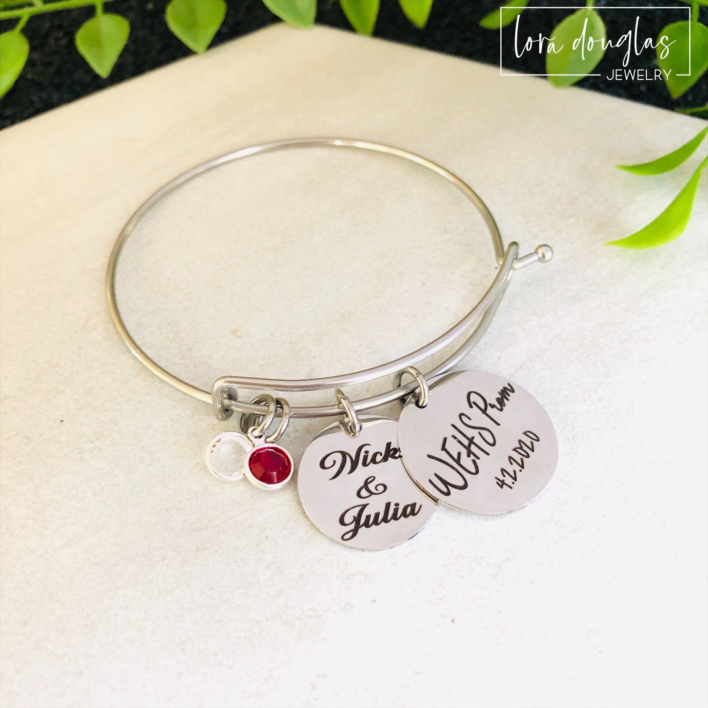 A stainless steel bangle bracelet with personalized engravings, presented in a blue box with 'Promposal' text.