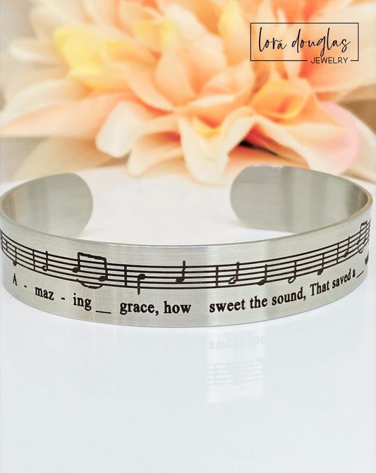 Celebrate the timeless beauty of "Amazing Grace" with this elegant sheet music bracelet. Featuring a delicate 1/2" width band engraved with the song’s iconic notes, it’s a meaningful gift for musicians, choir members, or anyone touched by this classic hymn. Perfect for recitals, piano players, or music lovers, this bracelet combines style and sentiment in a wearable keepsake. Give a gift that speaks to the heart and honors the power of music.