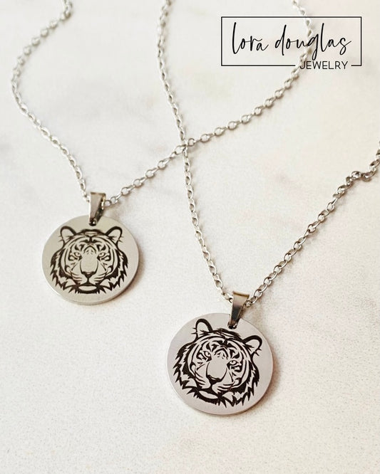Two pieces of jewelry, a necklace and a bracelet, featuring round pendants with a black and white tiger design on a silver-colored background.