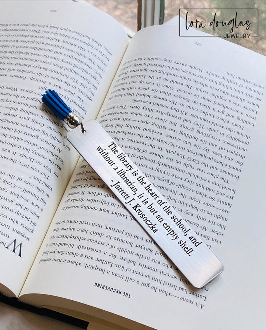 engraved metal bookmark with custom wording displayed beside an open book, personalized stainless steel bookmark with tassel and permanent engraving, ideal for teacher appreciation and reader gifts