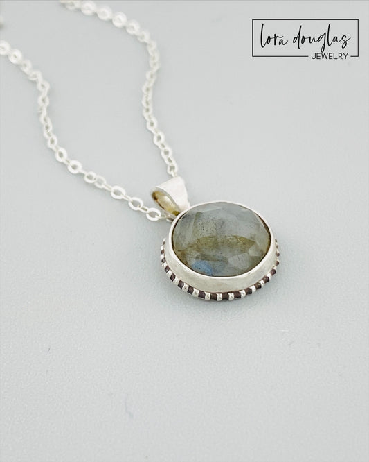 A sterling silver pendant necklace with a faceted labradorite gemstone in the center, attached to an 18-inch chain with a C clasp.