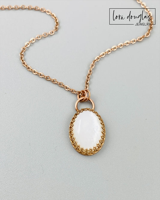 A bronze necklace with a stainless steel chain featuring a round moonstone pendant in a bronze setting.
