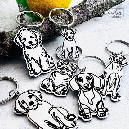 Dog-shaped keychains on a light surface. Close up of engraved stainless steel dog breed keychains showing detailed laser engraved dog silhouettes.
