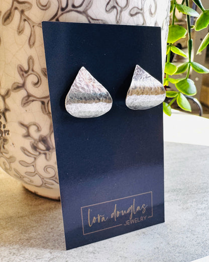 Teardrop-shaped sterling silver earrings on a Lora Douglas Jewelry card with a plant in the background.