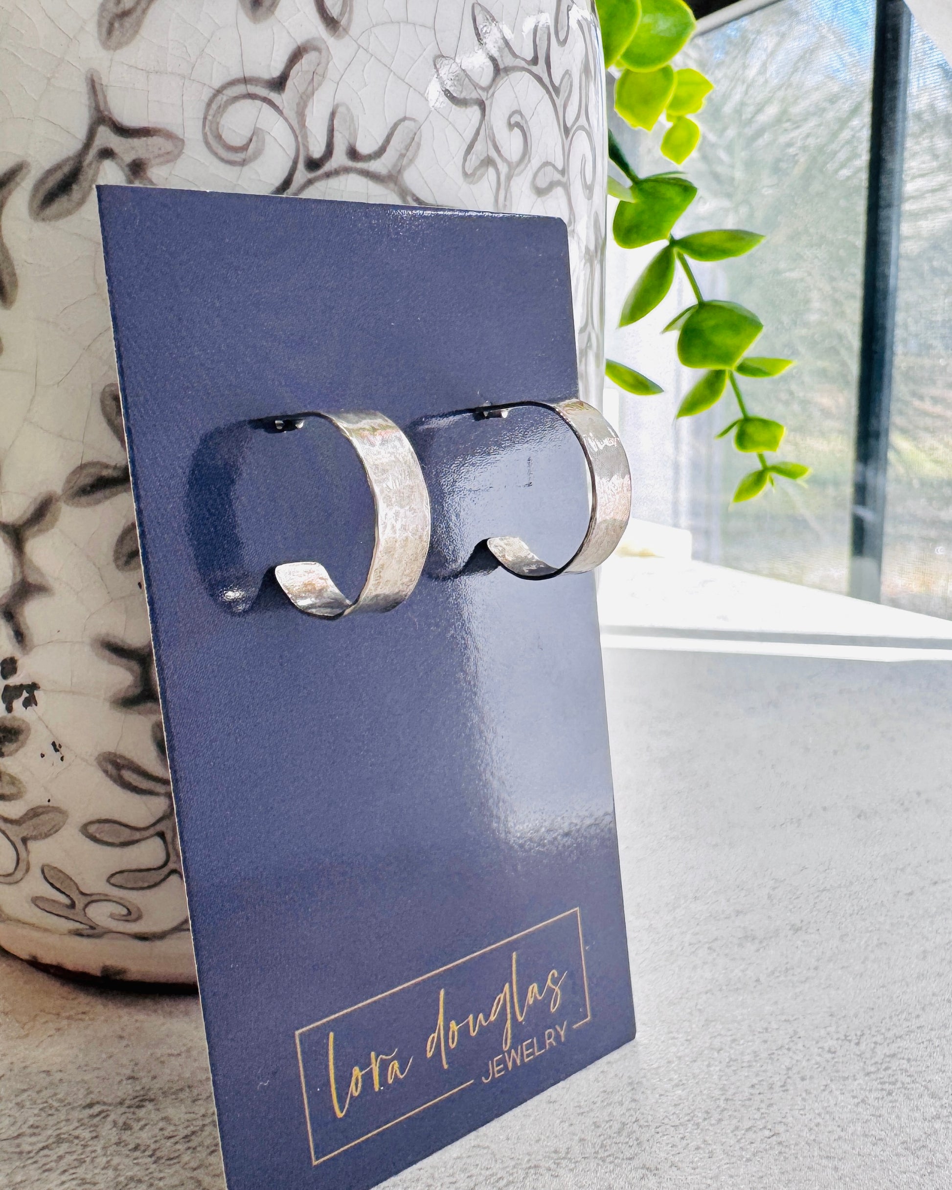 Pair of silver earrings on a blue card with 'Lora Douglas Jewelry' branding, against a neutral background.