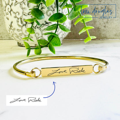 A gold  bangle bracelet with the engraved handwriting 