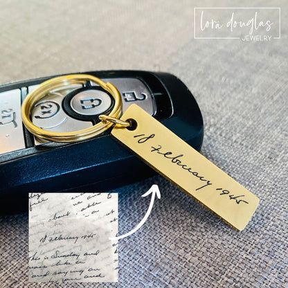 A gold stainless steel keychain with engraved handwriting on a car key.