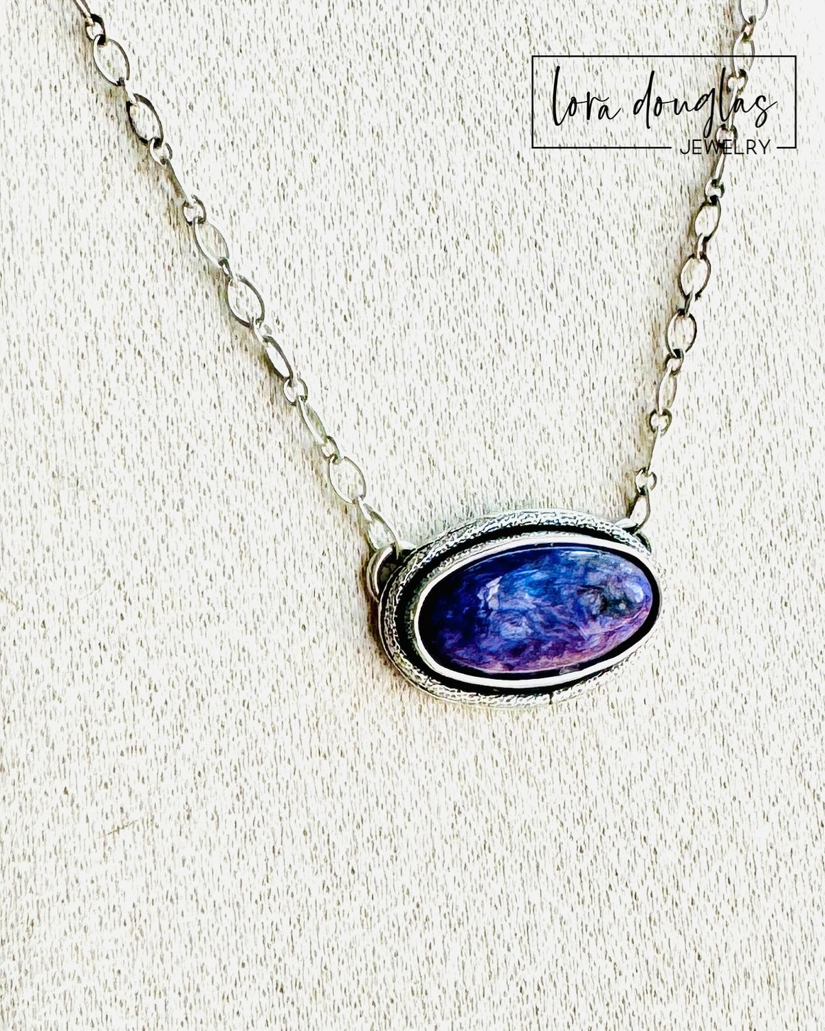 Close view of a natural charoite pendant highlighting the rich purple coloring and individual pattern variation of the oval gemstone, set in sterling silver for a classic natural stone necklace.
