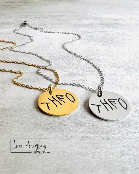 Comparison of sterling silver and stainless steel handwriting jewelry options showing custom engraved round pendants. Personalized keepsake jewelry available as a charm, necklace, or bracelet with permanent engraving.