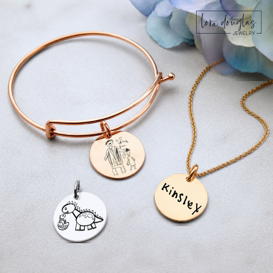 Custom child art jewelry featuring a child's actual drawing permanently laser engraved onto a round stainless steel pendant, available in silver, gold, or rose gold as a personalized keepsake necklace, charm, or bracelet.
