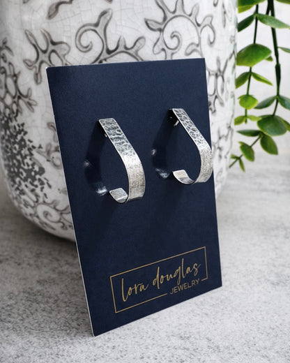 Sterling silver hoop earrings on a Lora Douglas Jewelry card with a decorative vase and plant in the background.