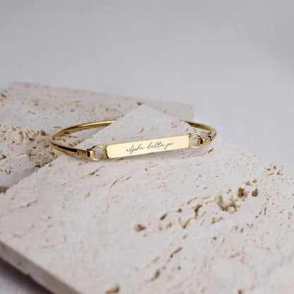 Gold bracelet with engraved text on a light stone surface