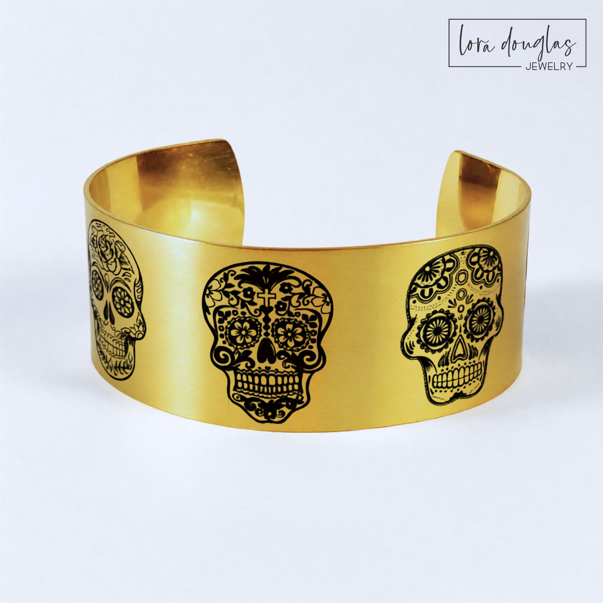 Gold stainless steel sugar skull cuff bracelet featuring five unique engraved skull designs around the wide band, with a matte gold finish for a bold statement piece inspired by traditional sugar skull artwork.
