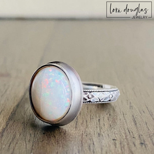 Handcrafted opal ring featuring a 10mm x 12mm hand cut oval cabochon in a .925 sterling silver bezel setting, shown as a finished US size 7.75 ring for shoppers looking for artisan gemstone jewelry.
