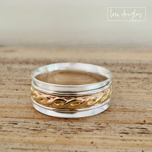 Handcrafted sterling silver and gold filled spinner ring featuring a wide silver band with a decorative gold center spinner, designed as elegant mixed metal fidget jewelry for everyday wear.
