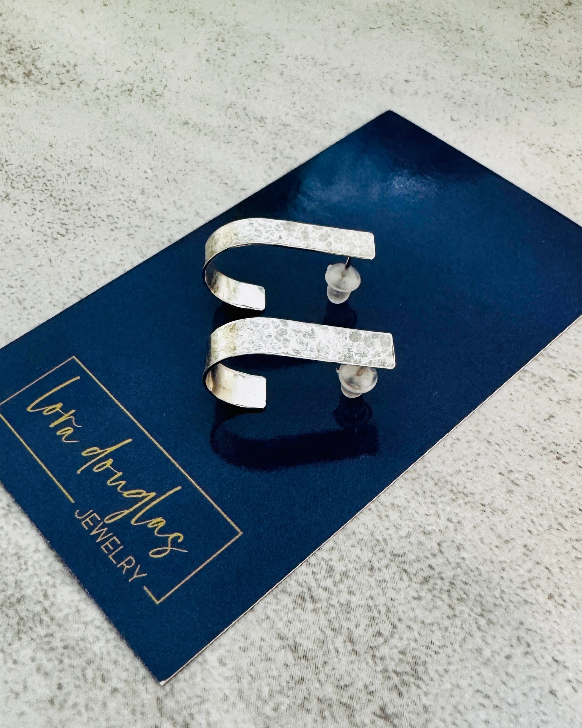 Silver earrings on a blue card with 'Lora Douglas Jewelry' branding.