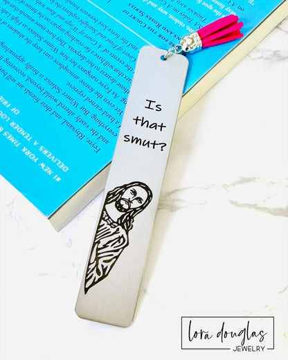 Is that smut bookmark. A stainless steel bookmark with  a leather tassel, featuring a laser engraving of a Jesus character with the text Is that Smut?