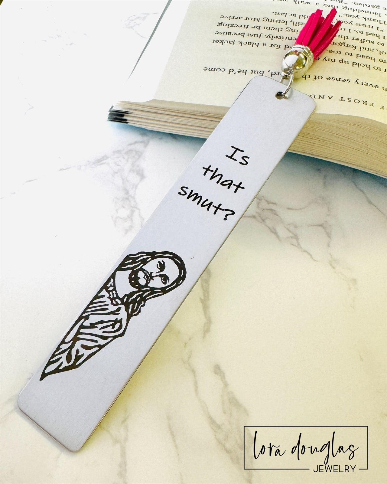 A stainless steel bookmark with  a leather tassel, featuring a laser engraving of a Jesus character with the text Is that Smut?
