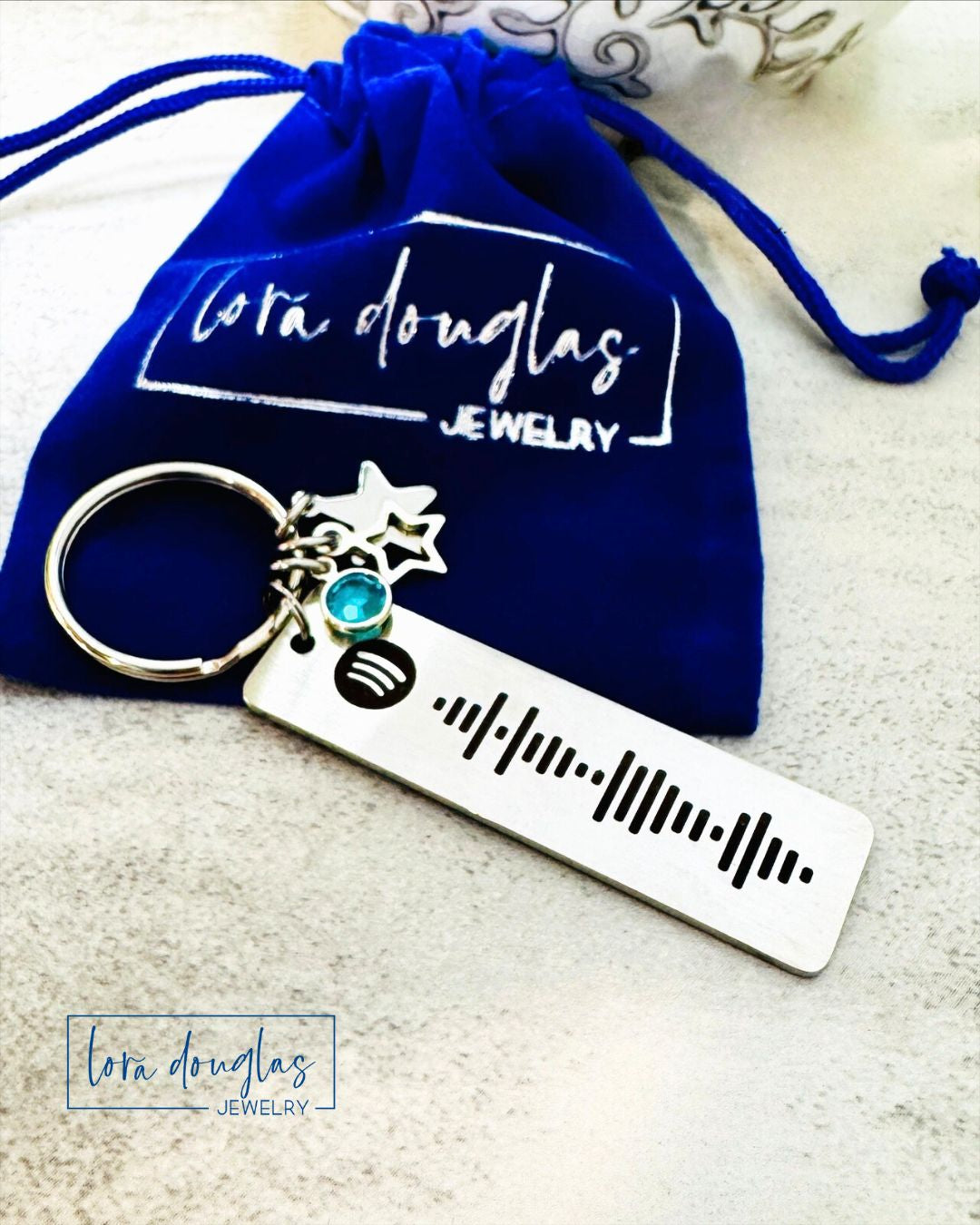 A stainless steel keychain with a custom  laser engraved Spotify code, displayed next to blue gift bag