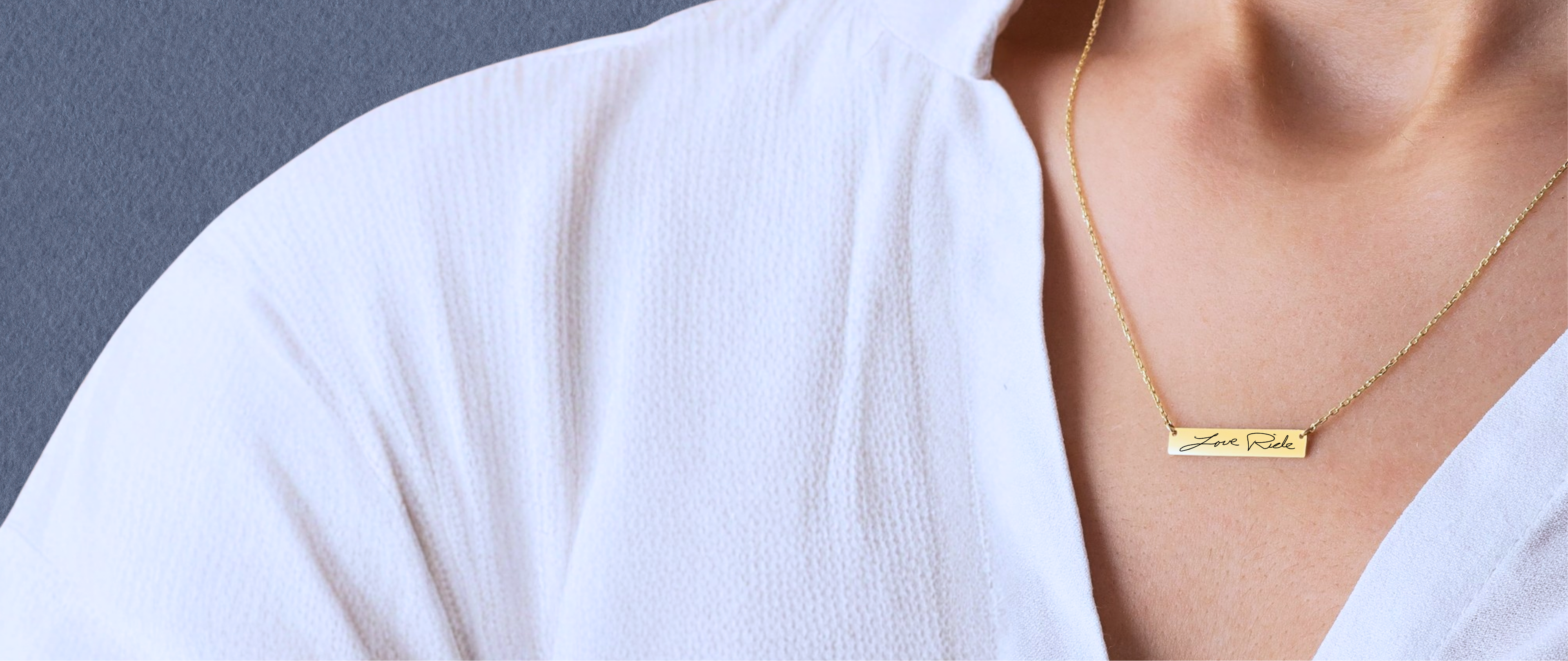 Gold necklace with a bar pendant engraved with real handwriting on a person wearing a white shirt against a gray background