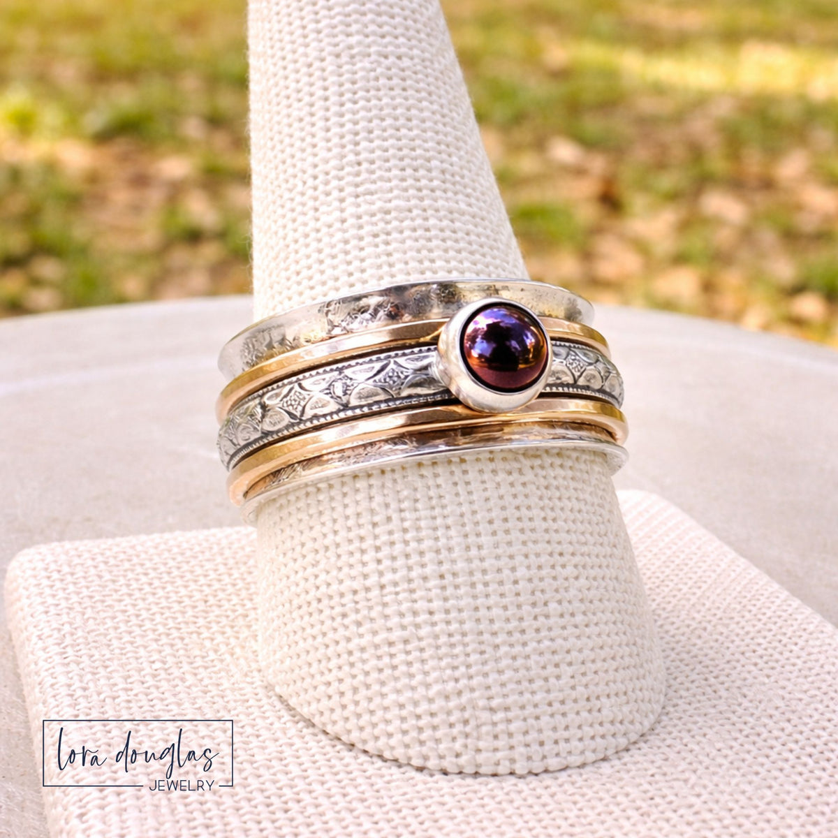 A bold, grounding piece with movement and texture. This handcrafted spinner ring features a wide sterling silver band layered with gold filled accents and a deep garnet stone that catches the light beautifully.