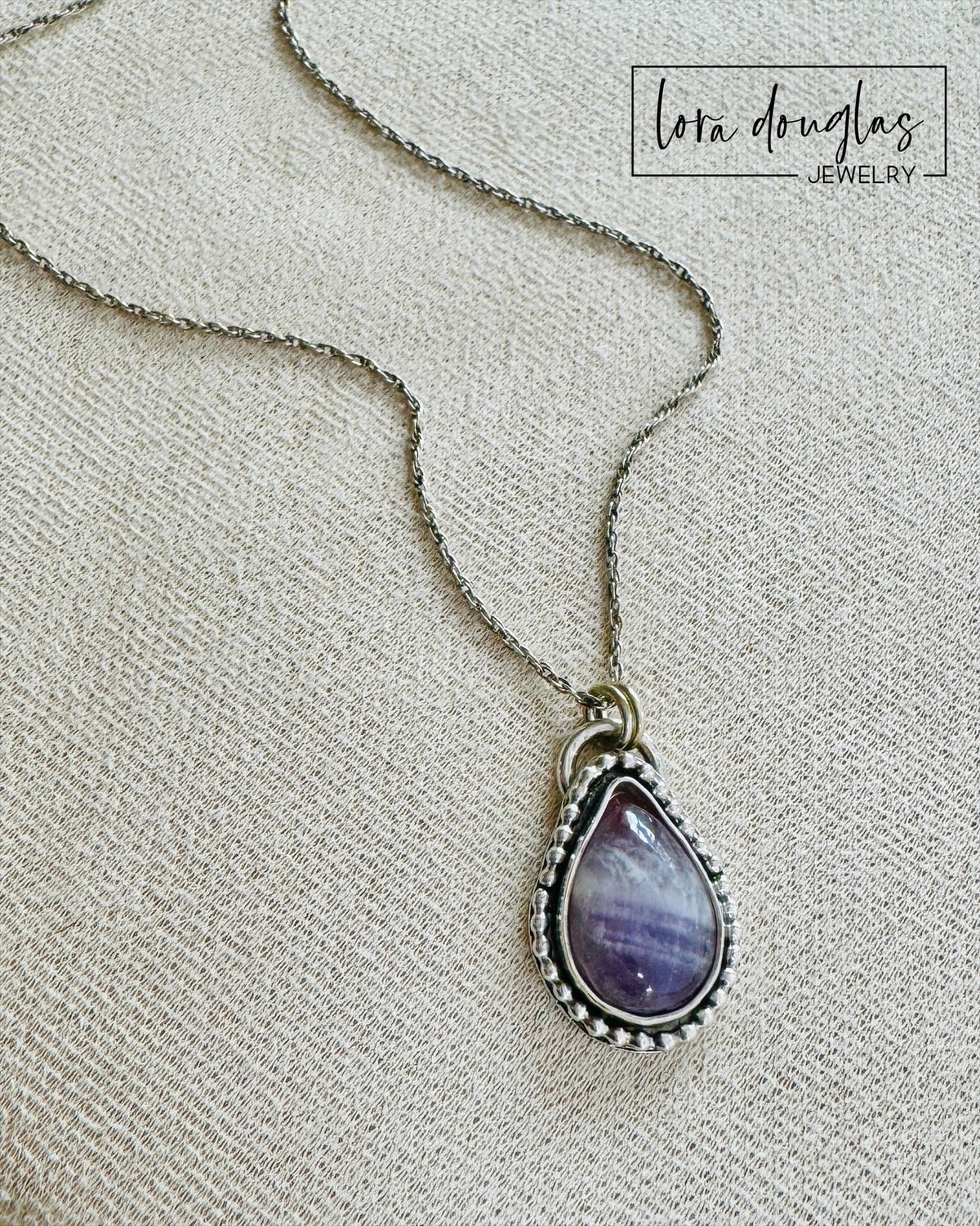 Natural banded amethyst necklace featuring a teardrop gemstone with distinctive purple coloring and natural patterning, set in 925 sterling silver and paired with an 18 inch chain for an easy to wear gemstone pendant.

