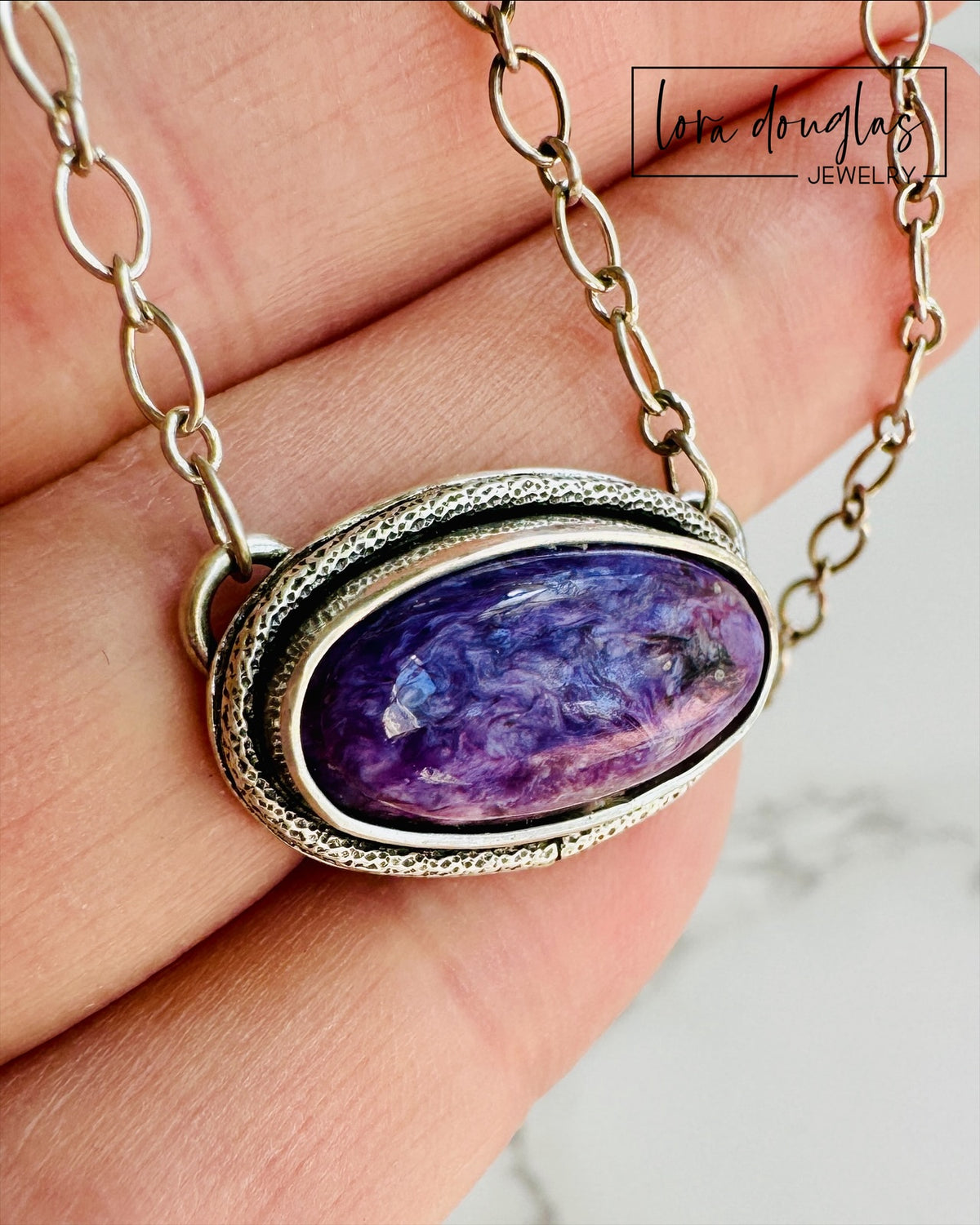 Natural charoite necklace featuring an oval purple gemstone set in 925 sterling silver and paired with an approximately 20 inch chain, showcasing the distinctive coloring and pattern variation of the stone.
