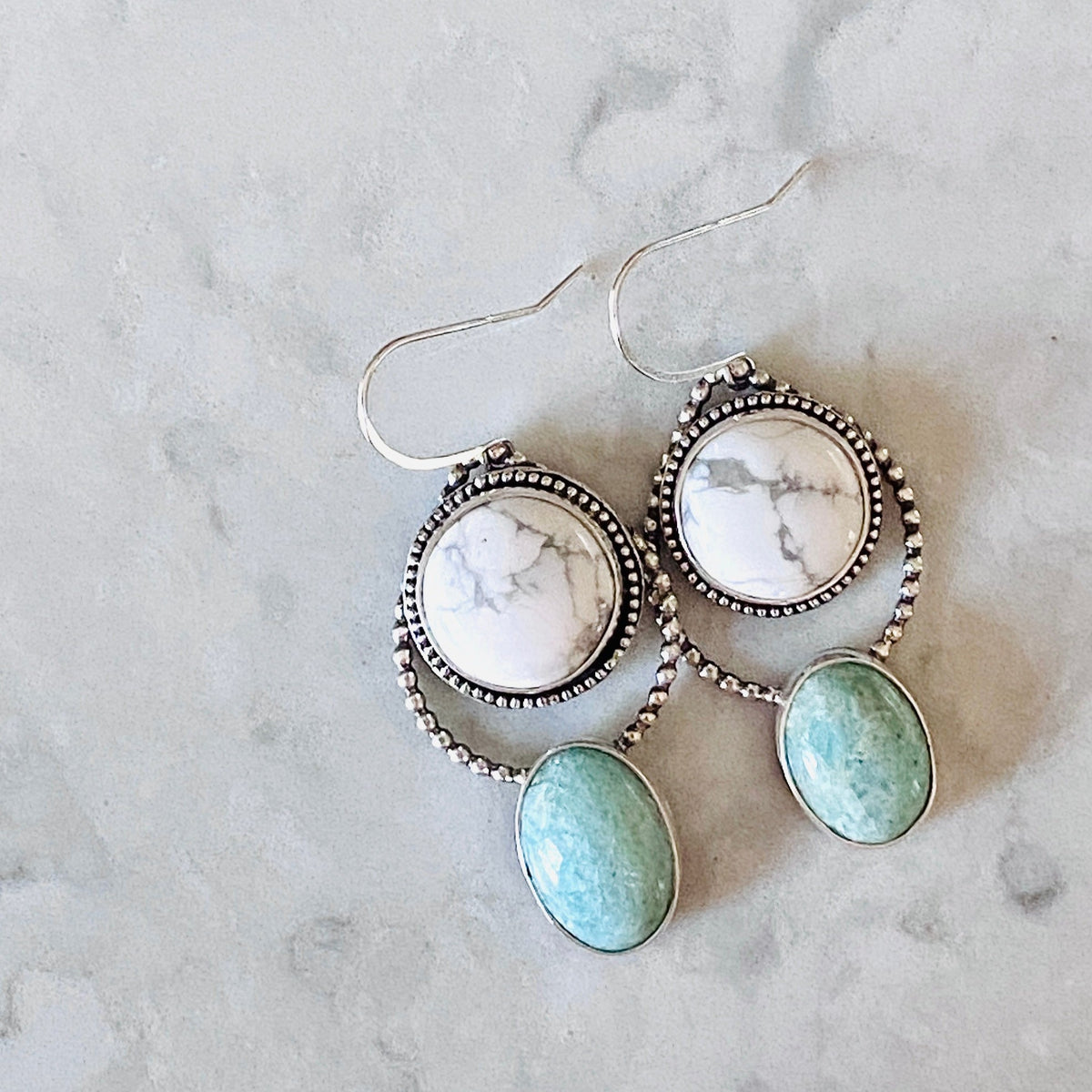 Natural stone earrings with oval howlite and amazonite gemstones set in sterling silver, featuring white marbled and pale green stones in a long articulated dangle style that adds movement when worn.
