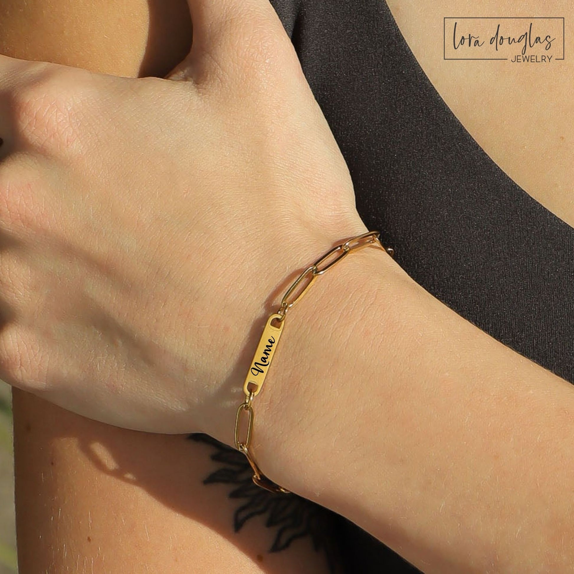 Gold bracelet with engraved name on wrist, Lora Douglas Jewelry branding.