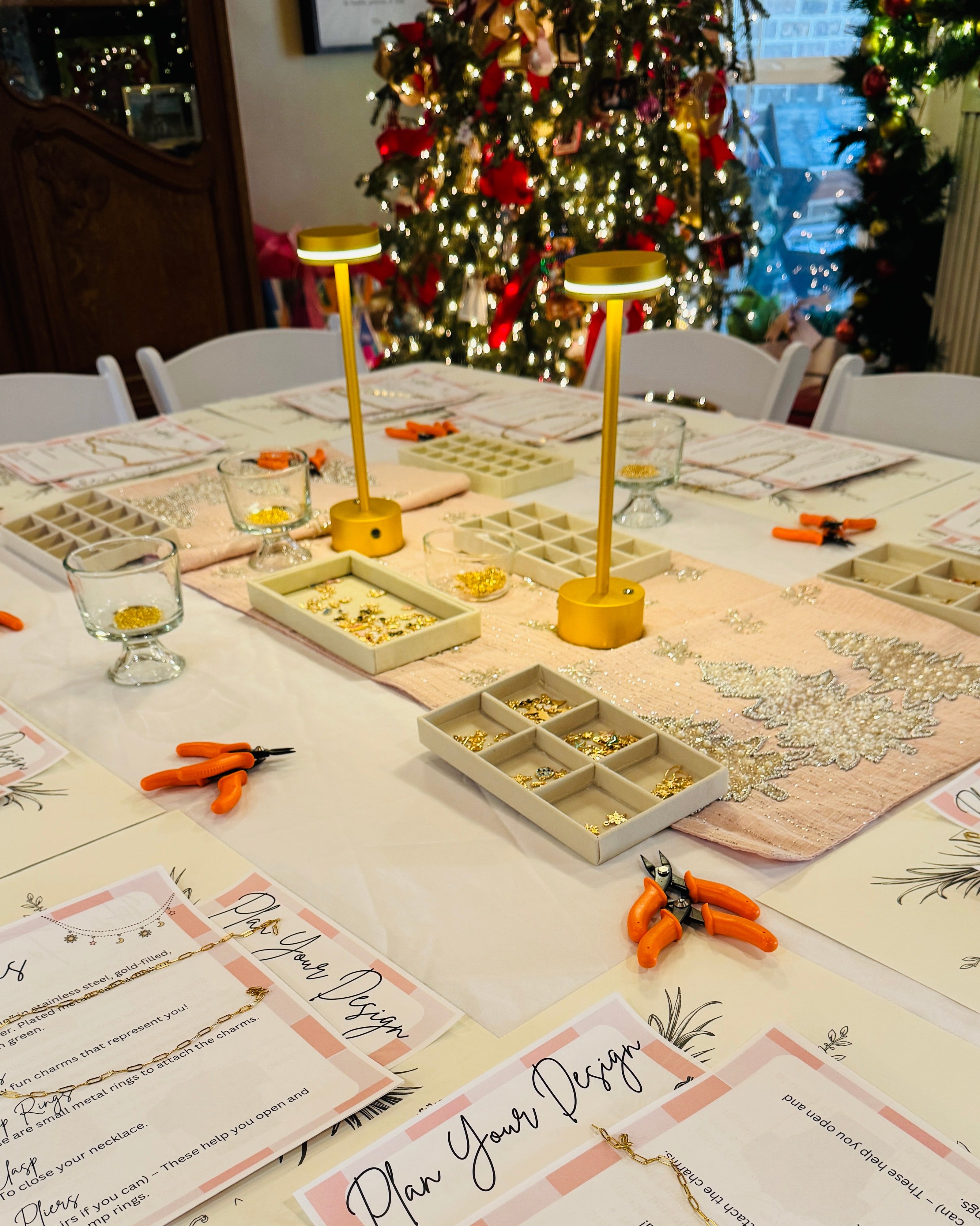 Table with jewelry-making supplies and templates in front of a decorated Christmas tree.