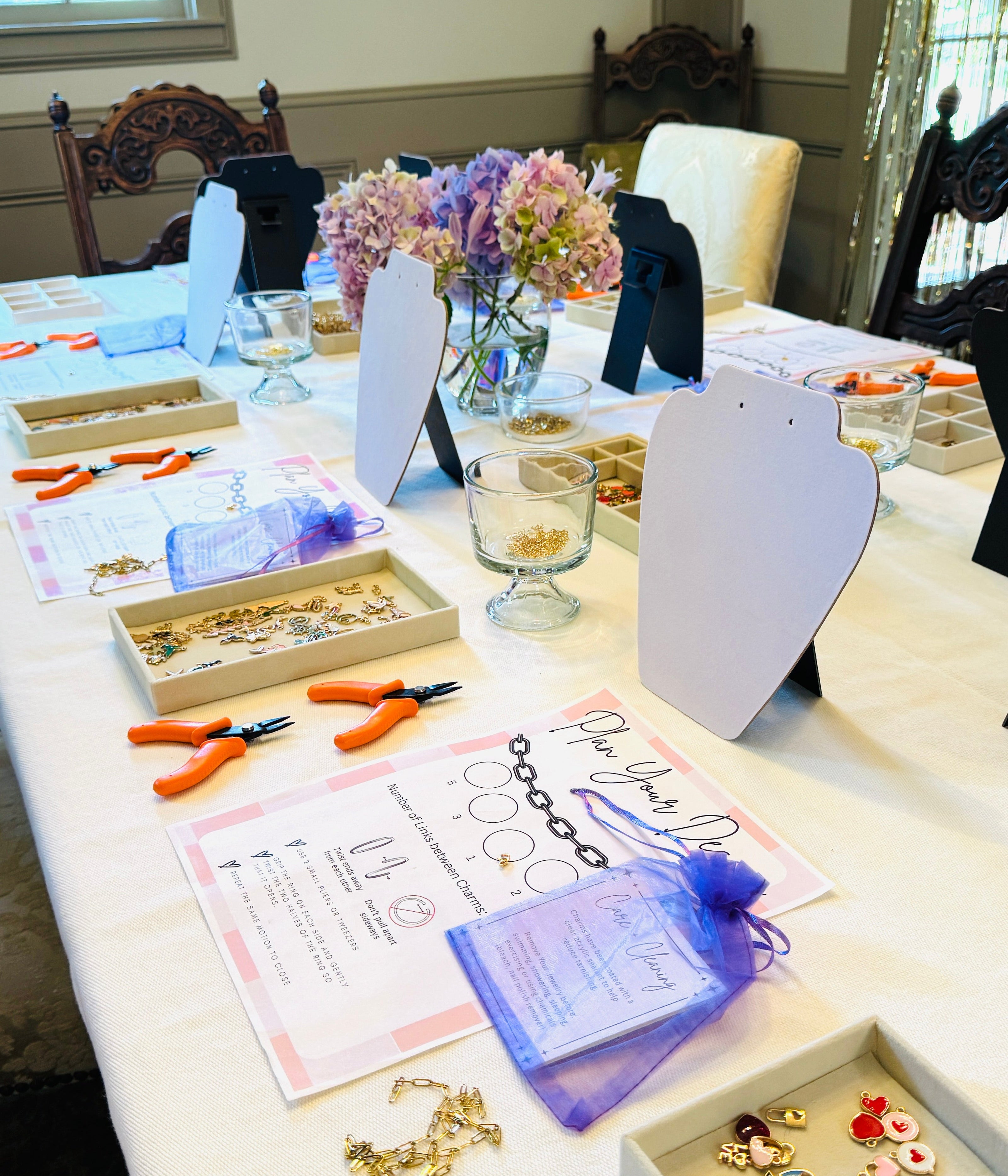 Table with jewelry-making supplies and materials in a room with chairs and a window.