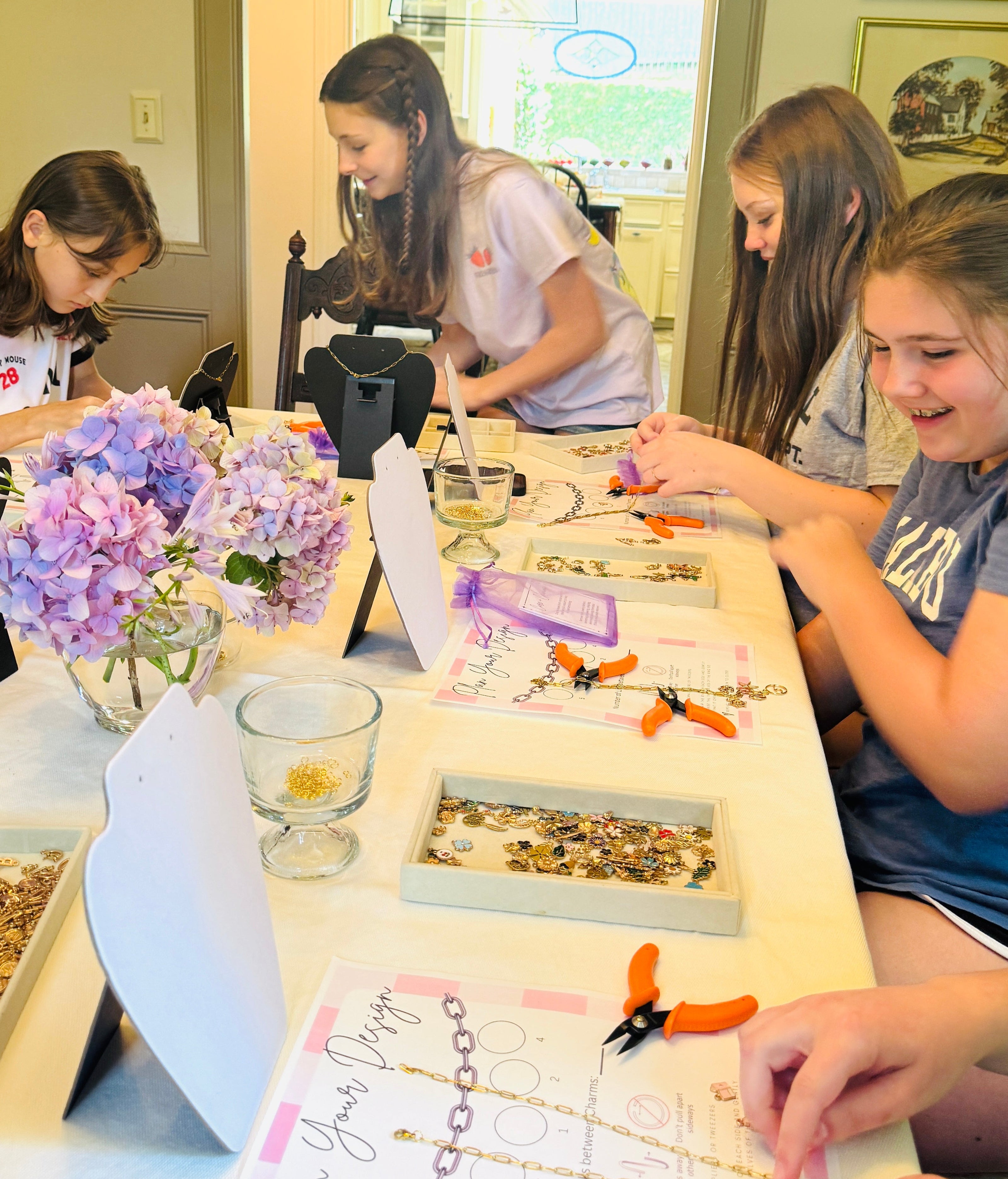 Group of people at a table making jewelry with supplies and balloons in the background.