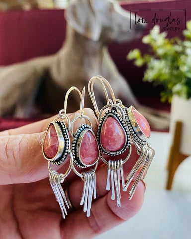 Pink teardrop earrings with silver fringe on a hand, blurred background