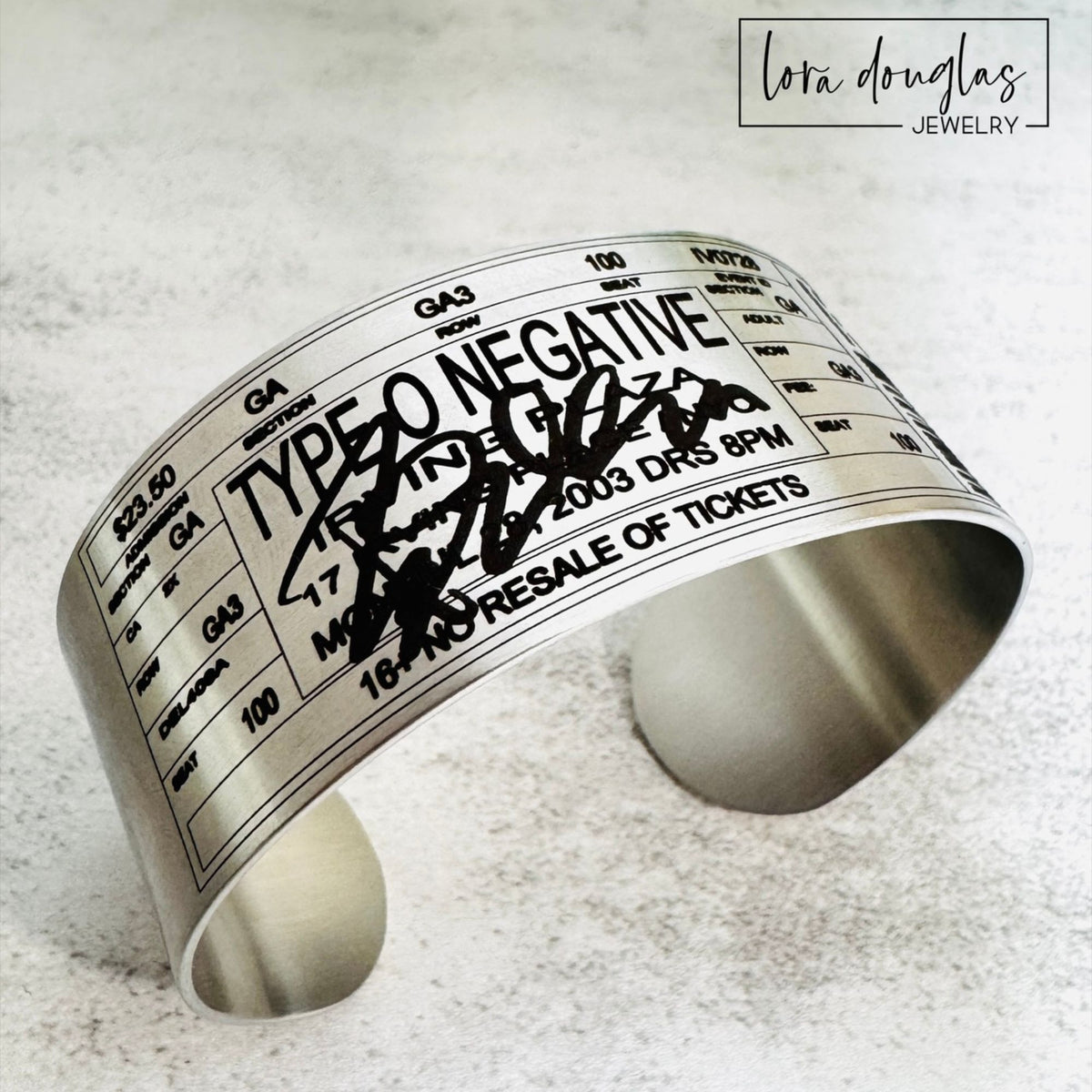 Silver or gold personalized concert bracelet designed to resemble an event ticket, with space for custom artist, tour, location, date, section, row, seat, price and a short personalized message.
