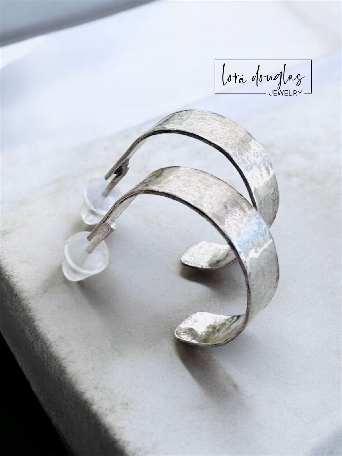 Small hammered silver hoop earrings crafted from sterling silver with matching silver posts, featuring a textured light catching finish for shoppers who prefer understated earrings with handcrafted character.
