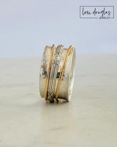 Stack of gold and silver rings on a light surface with 'Lota Douglas Jewelry' branding.