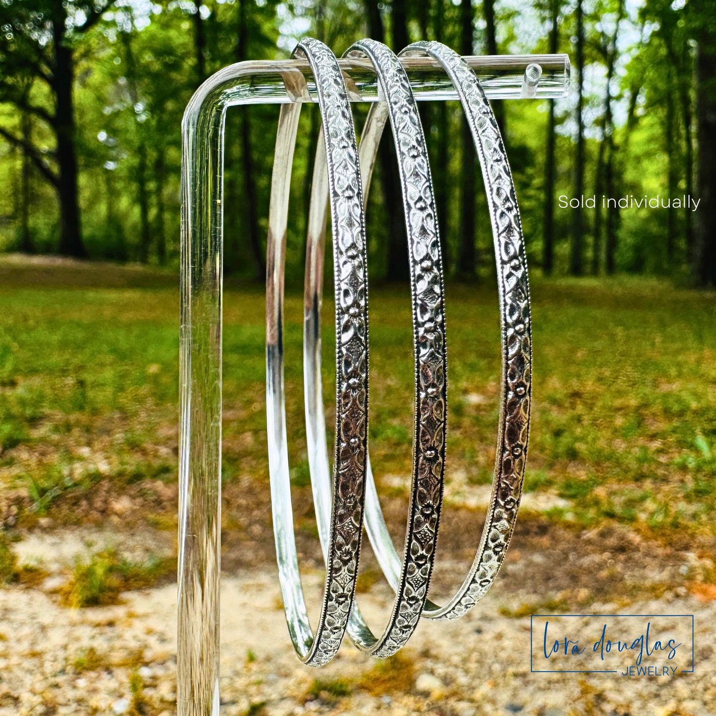Three sterling silver bangles on a stand with a natural background