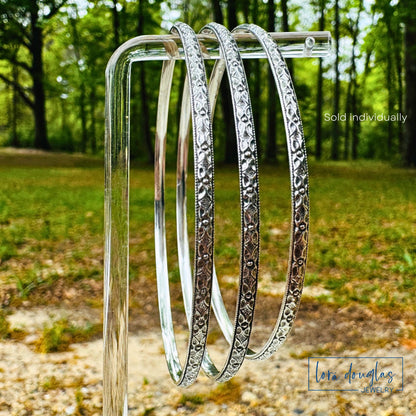 Three sterling silver bangles on a stand with a natural background
