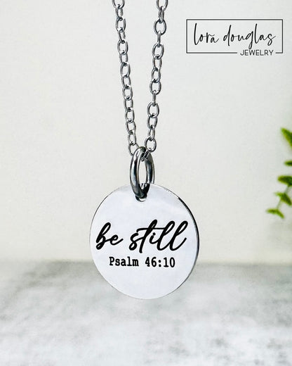 Necklace with a pendant that reads 'be still Psalm 46:10' on a light background.