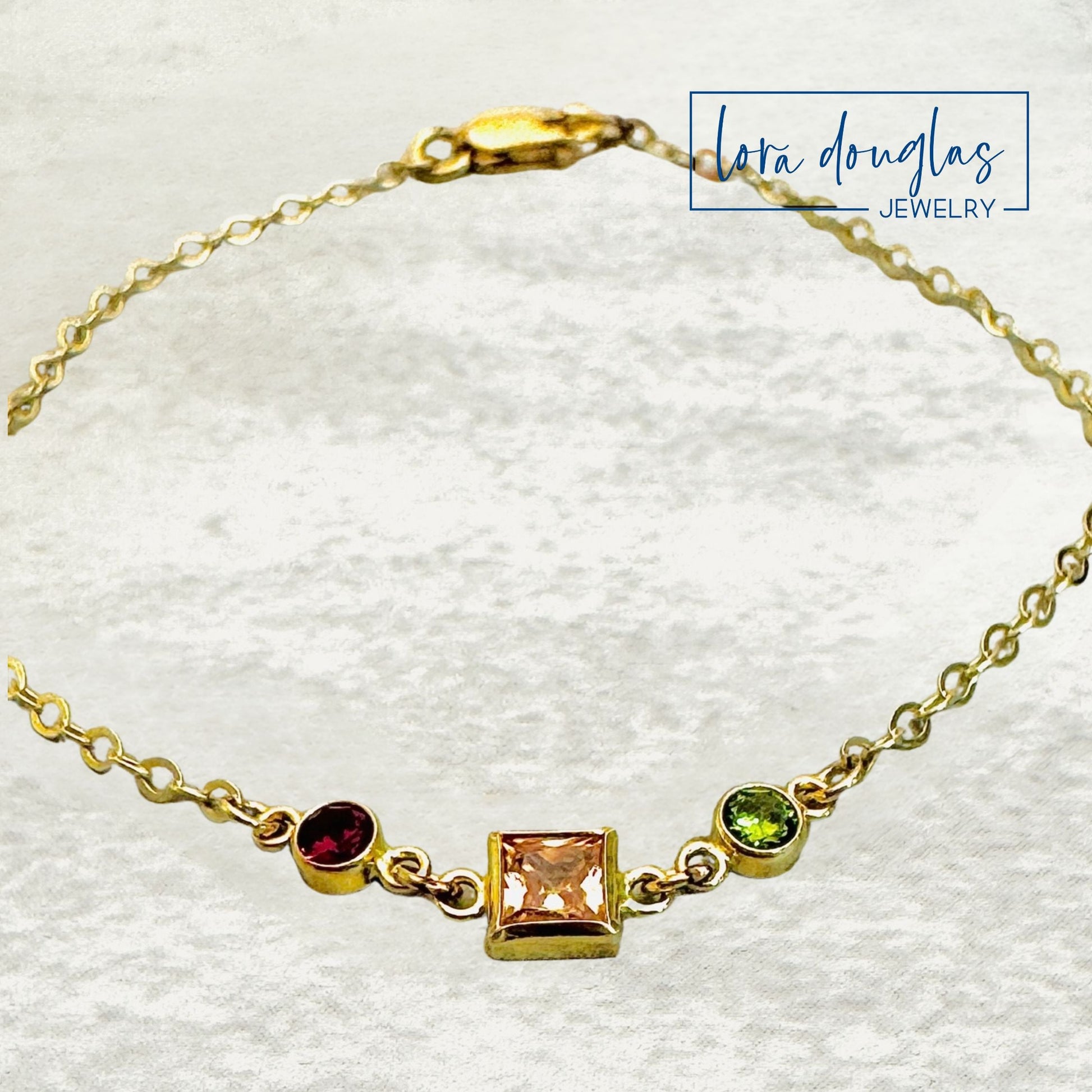 Gold bracelet with gemstones on a white background, featuring the brand 'Lora Douglas Jewelry'.