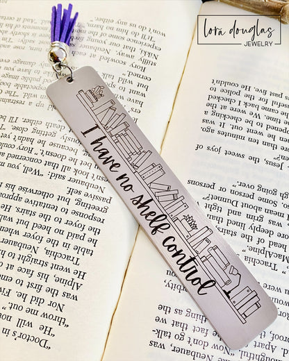 A stainless steel bookmark with an engraving that reads 'I HAVE NO SHELF CONTROL' on a bookshelf background, placed on an open book.