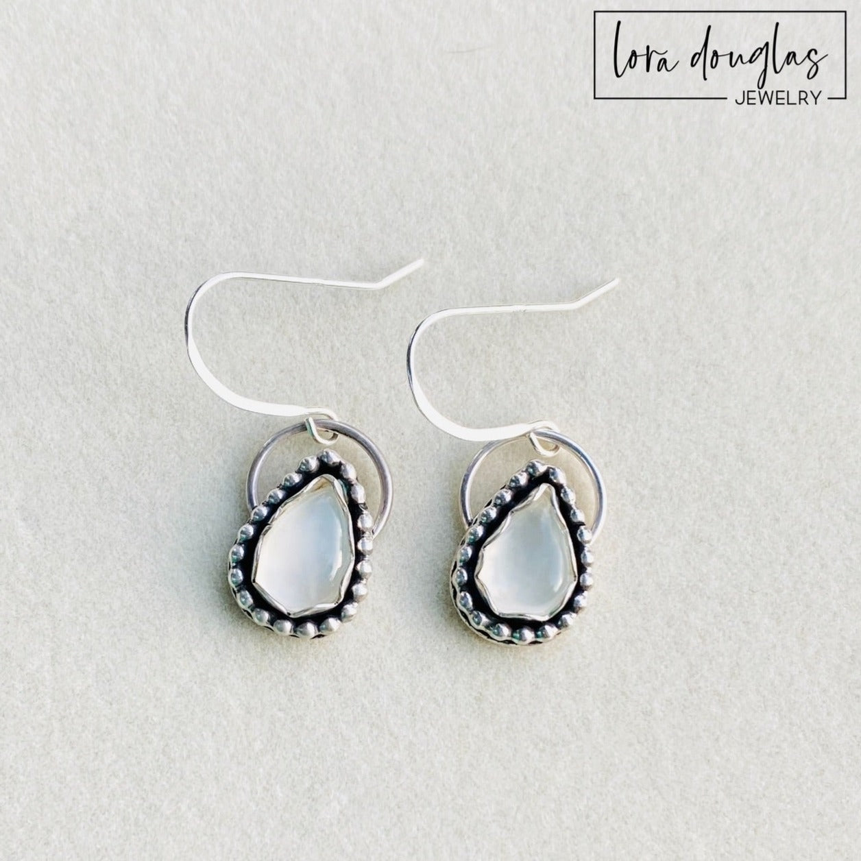 A pair of sterling silver dangle earrings with a teardrop-shaped moonstone stone in the center