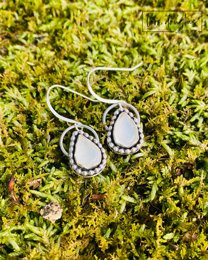A pair of sterling silver dangle earrings with a teardrop-shaped moonstone stone in the center